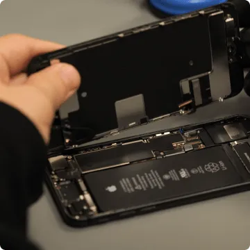 Un smartphone ouvert par l'arrière. Le pouce et l'index soulèvent la face arrière vers le haut, révélant la batterie du téléphone portable d'occasion.